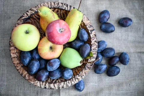 Assorted fresh plums, apples, and pears in a rustic wooden bowl. Great backgroun Stock Photos