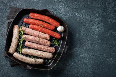 Assorted fresh raw sausages with thyme, rosemary and garlic in a cast iron pa Stock Photos