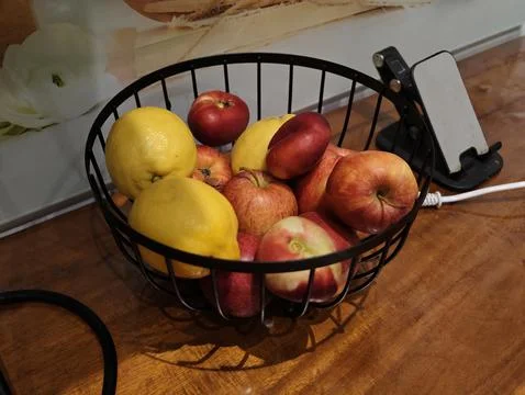 Assorted fruit in black wire bowl on wooden table Foto stock