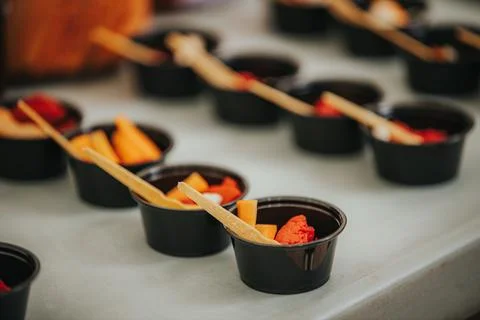 Assorted fruit samples in black plastic cups with wooden spoons arranged on.. Stock Photos