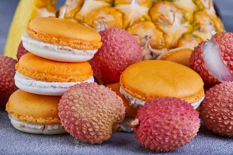 Assorted fruits like pineapple, lychee, and macarons displayed on a table Stock Photos