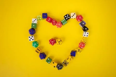 Assorted game dice in the shape of a heart on yellow background Stock Photos