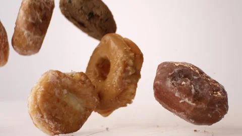 Assorted glazed and chocolate cake donuts bouncing on white slow motion macro Stock Footage 336707003