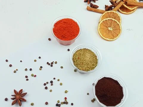 Assorted ground spices in containers with dried orange and cinnamon on white Stock Photos