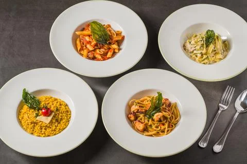 Assorted Italian pasta and risotto dishes arranged on a dark table Stock Photos