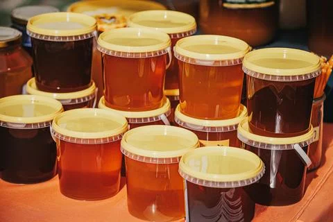 Assorted jars of honey with yellow lids arranged on a table, showcasing var.. Stock Photos