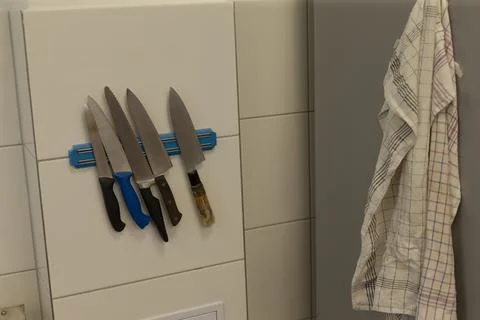 Assorted kitchen knives on blue magnetic rack mounted on tiled wall with towels Stock Photos