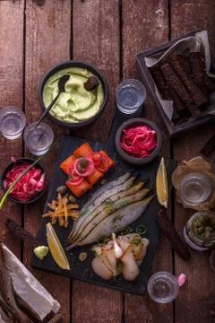 Assorted marinated fish on dark cutting board with vodka shots. Stock Photos