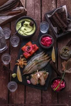Assorted marinated fish on dark cutting board with vodka shots. Stock Photos