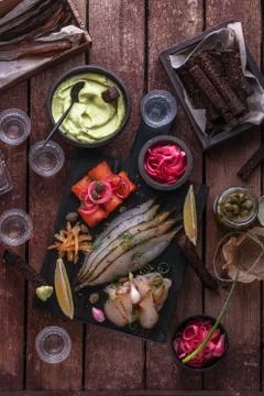 Assorted marinated fish on dark cutting board with vodka shots. Stock Photos
