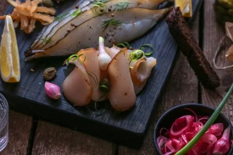 Assorted marinated fish on dark cutting board with vodka shots. Stock Photos