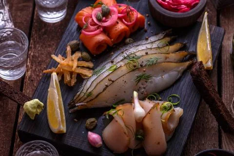 Assorted marinated fish on dark cutting board with vodka shots. Stock Photos
