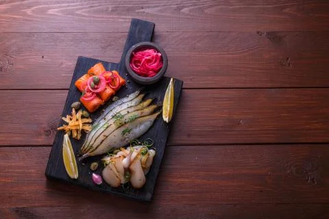 Assorted marinated fish on dark cutting board, copy space Stock Photos