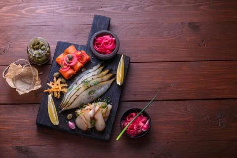 Assorted marinated fish on dark cutting board, copy space Stock Photos