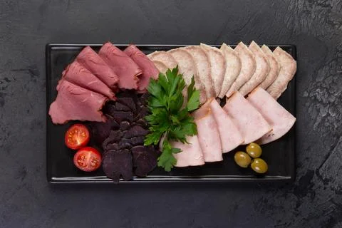 Assorted meat delicacies on a dark background. Stock Photos