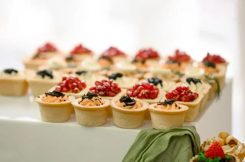 Assorted mini desserts with fruit toppings arranged on a white display Stock Photos