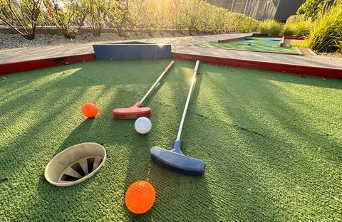 Assorted miniature golf putters and balls askew on synthetic grass. Stockfoto's