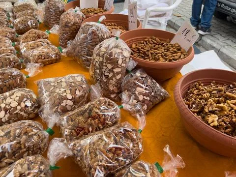 Assorted nuts and almonds displayed in bags and bowls at outdoor market stall Stock Photos