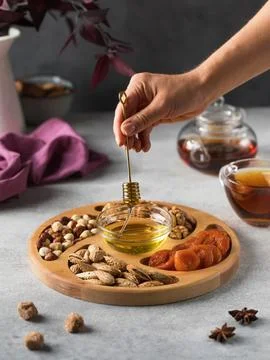 Assorted nuts and dried apricots on a wooden plate with honey and a mug of tea. Stock Photos