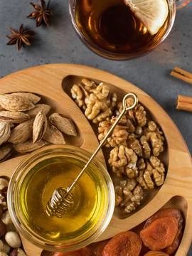 Assorted nuts and dried apricots on a wooden plate with honey and a mug of tea. Foto stock