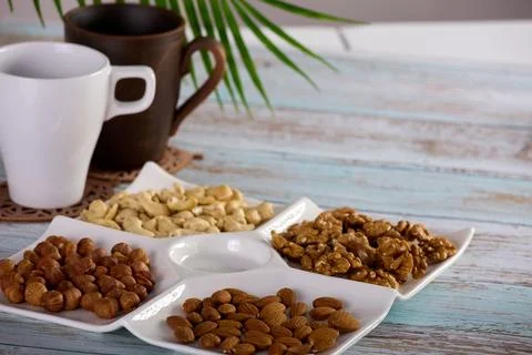 Assorted nuts are laid out on square-shaped plate along with empty glasses Stock Photos