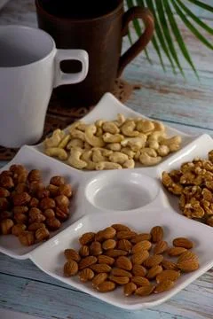 Assorted nuts are laid out on square-shaped plate along with empty glasses Stock Photos