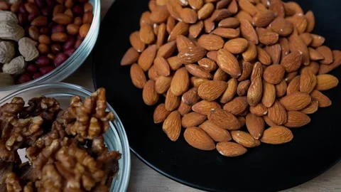 Assorted nuts including almonds, walnuts, and peanuts on plates Stock Footage 318578554