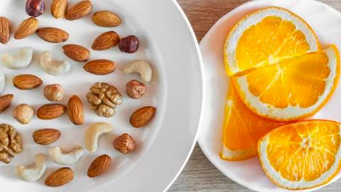 Assorted Nuts, Orange Slices On White Plates On Wooden Table. Healthy Organic Stock Photos