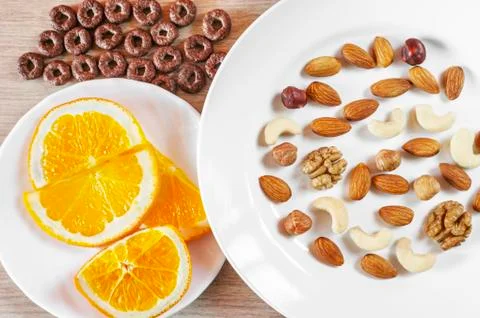 Assorted Nuts, Orange Slices On White Plates, Crunchy Whole Grain Cereals Rou Stock Photos