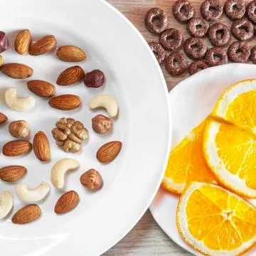 Assorted Nuts, Orange Slices On White Plates, Crunchy Whole Grain Cereals Rou Stock Photos