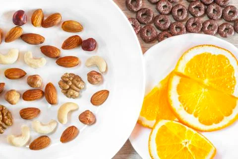 Assorted Nuts, Orange Slices On White Plates, Crunchy Whole Grain Cereals Rou Stock Photos