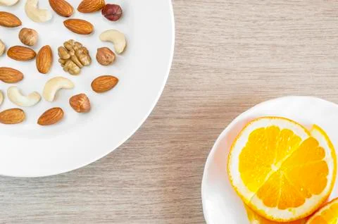 Assorted Nuts, Orange Slices On White Plates On Wooden Table. Healthy Organic Stock Photos
