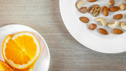 Assorted Nuts, Orange Slices On White Plates On Wooden Table. Healthy Organic Stock Photos