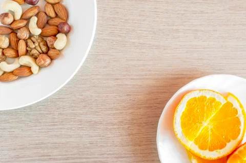 Assorted Nuts, Orange Slices On White Plates On Wooden Table. Healthy Organic Stock Photos
