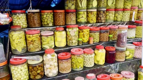 Assorted pickled fruits displayed in glass jars and trays. These tangy snacks Stock Footage 338319255