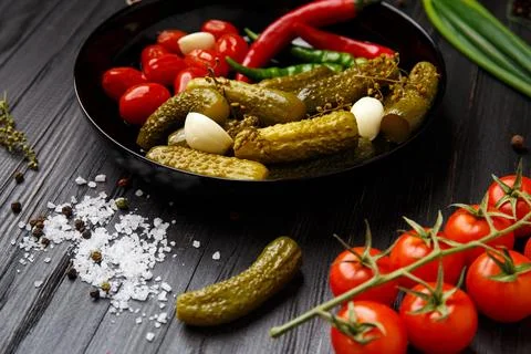 Assorted pickled vegetables in a black plate on a dark background. Stock Photos