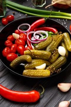 Assorted pickled vegetables in a black plate on a dark background. Stock Photos