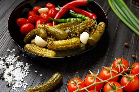 Assorted pickled vegetables in a black plate on a dark background. Stock Photos
