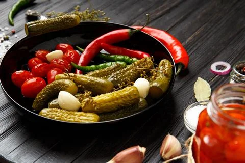 Assorted pickled vegetables in a black plate on a dark background. Stock Photos