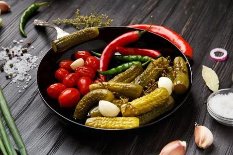Assorted pickled vegetables in a black plate on a dark background. Stock Photos