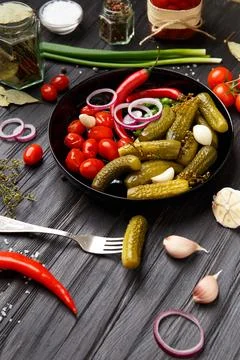 Assorted pickled vegetables in a black plate on a dark background. Stock Photos