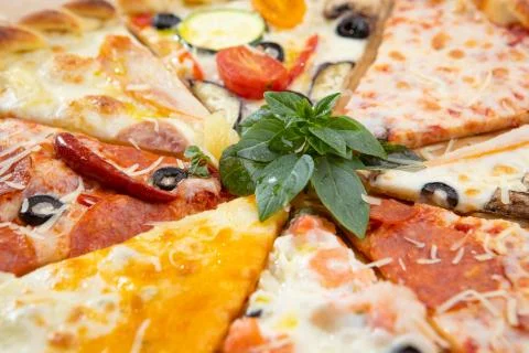 Assorted pieces of pizza closeup with different ingredients decorated with Basil Stock Photos
