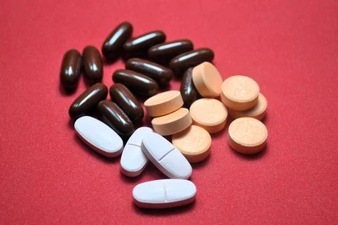 Assorted pills and tablets on red surface showcasing pharmaceutical variety.. Stock Photos