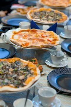 Assorted pizzas on table with plates and cups ready for dining Stock Photos