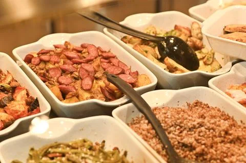Assorted prepared dishes fill white containers on buffet line inside self Stock Photos