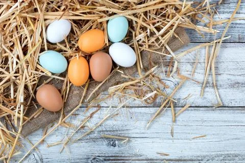 Assorted raw chicken eggs lying on straw and wooden background Stock Photos