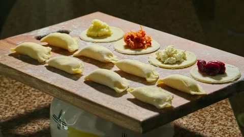 Assorted raw dumplings laid out on a board with flour, play with light Stock Footage 153805482