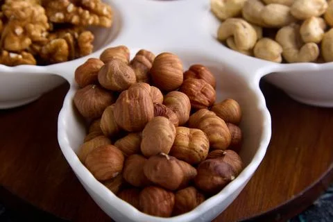 Assorted roasted and dried nuts are laid out in close-up on a white platter Stock Photos