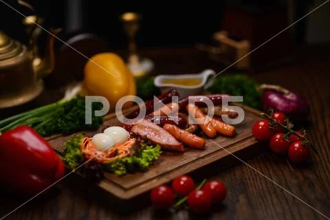 Assorted sausages and meat on a wooden plank, garnish of vegetables Stock Photos