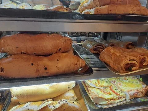 Assorted Savory Stuffed Breads, Ham Cachitos and Pizza in Bakery Showcase Stock Photos